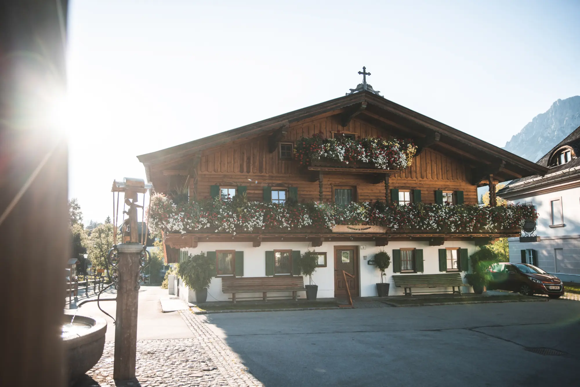 Der historische Gasthof Wilder Kaiser auf dem Dorfplatz in Going, ein traditionelles Tiroler Bauernhaus mit üppigem Blumenschmuck an den Holzbalkonen im Sommer.