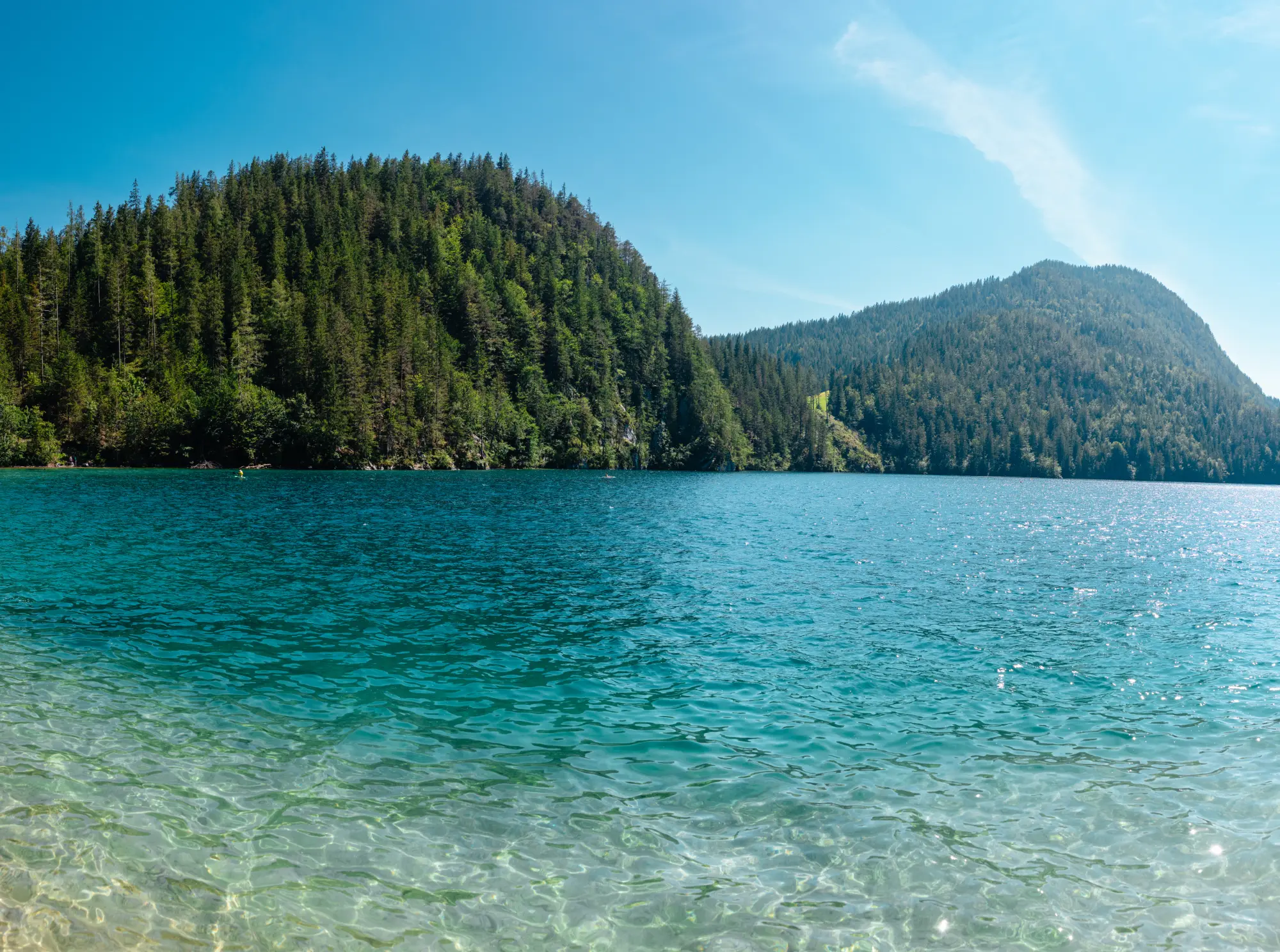 Kristallklares, türkisfarbenes Wasser des Hintersteiner Sees in der Region Wilder Kaiser in Tirol mit dicht bewaldeten Berghängen im Hintergrund.