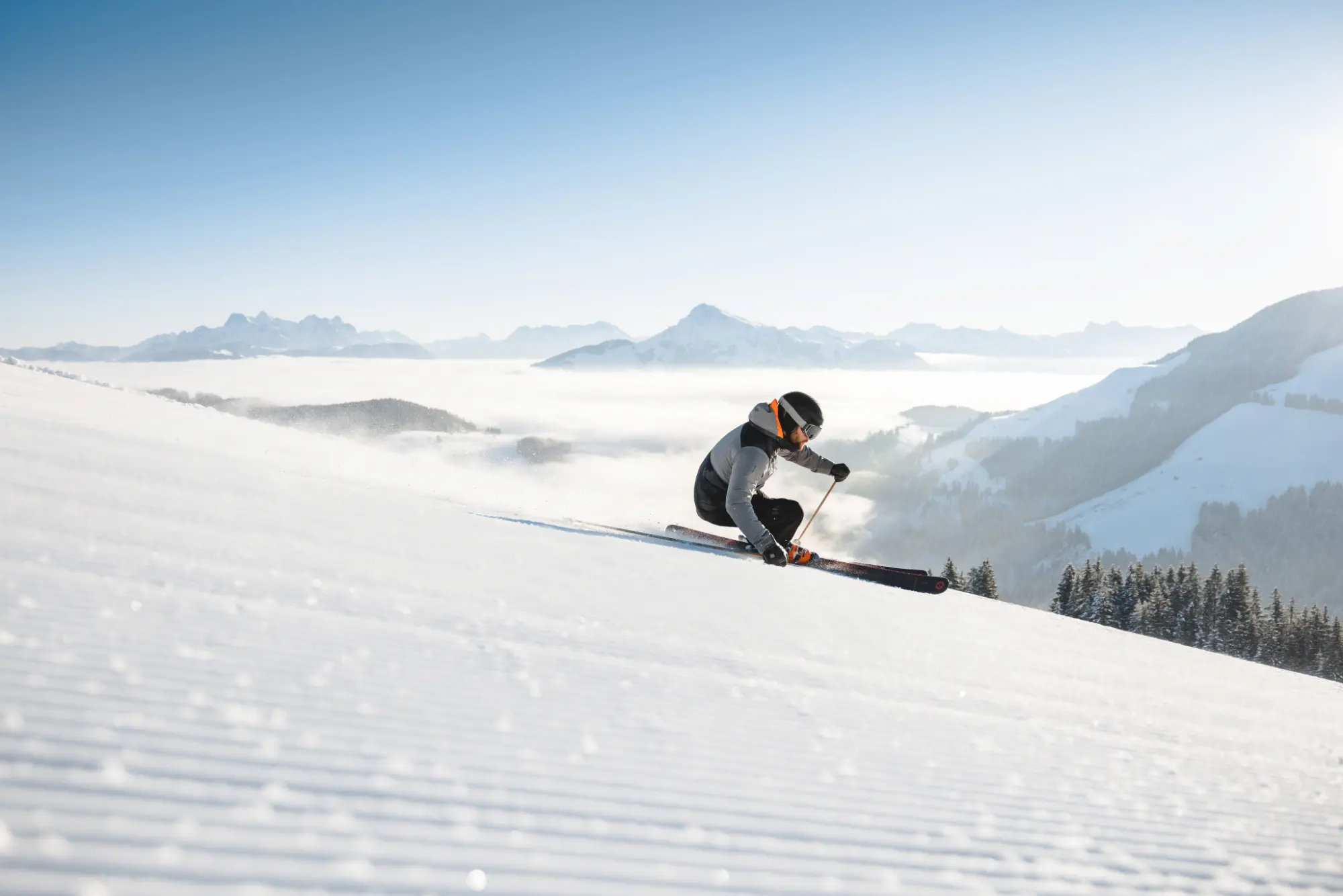 Ein Skifahrer in sportlicher Kurvenlage auf einer perfekt präparierten Piste mit typischem Rillenmuster im Skigebiet Wilder Kaiser in Tirol vor einer tief liegenden Wolkendecke.