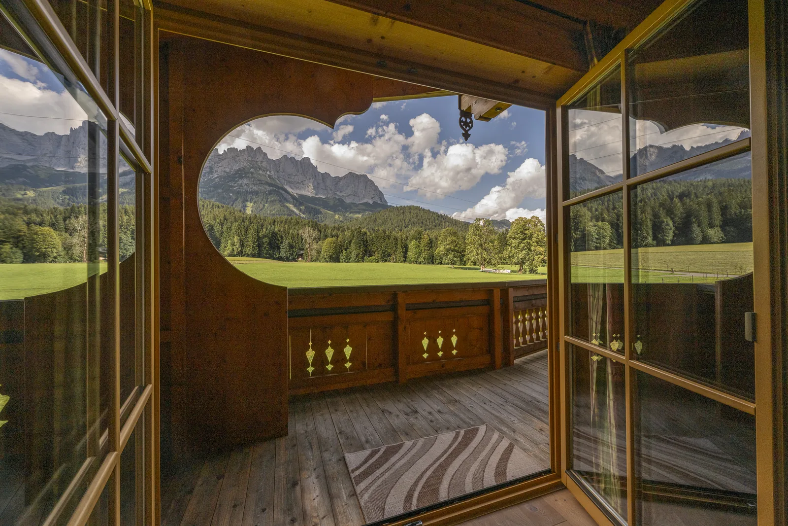 Blick vom Balkon durch die geschwungene Holzbrüstung auf den Wilden Kaiser
