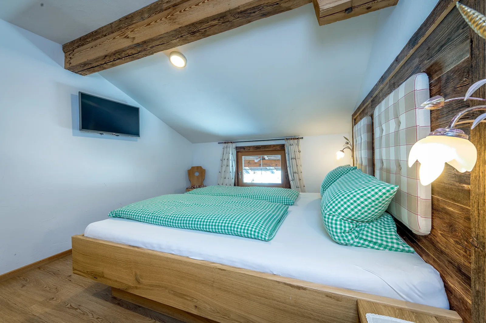 Schlafzimmer im Alpenblick unter der Dachschräge mit Altholzbalken und Fernseher