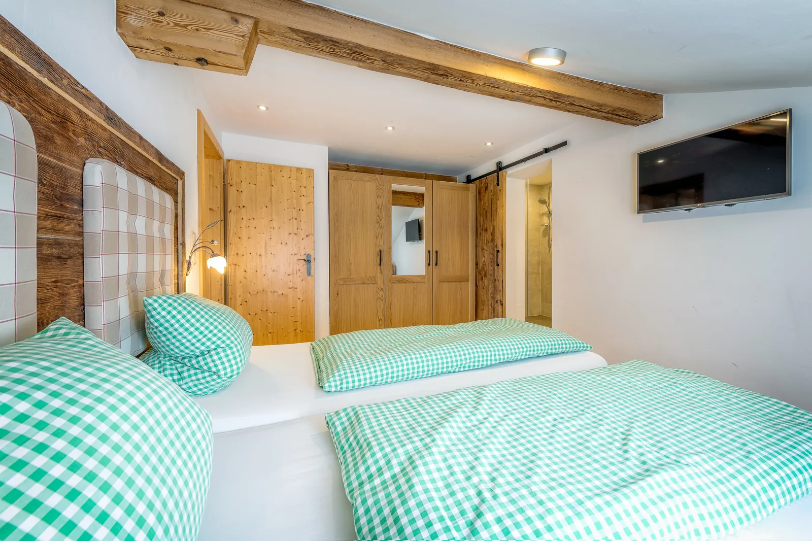 Schlafzimmer im Alpenblick mit Kleiderschrank, Fernseher und offenen Dachbalken
