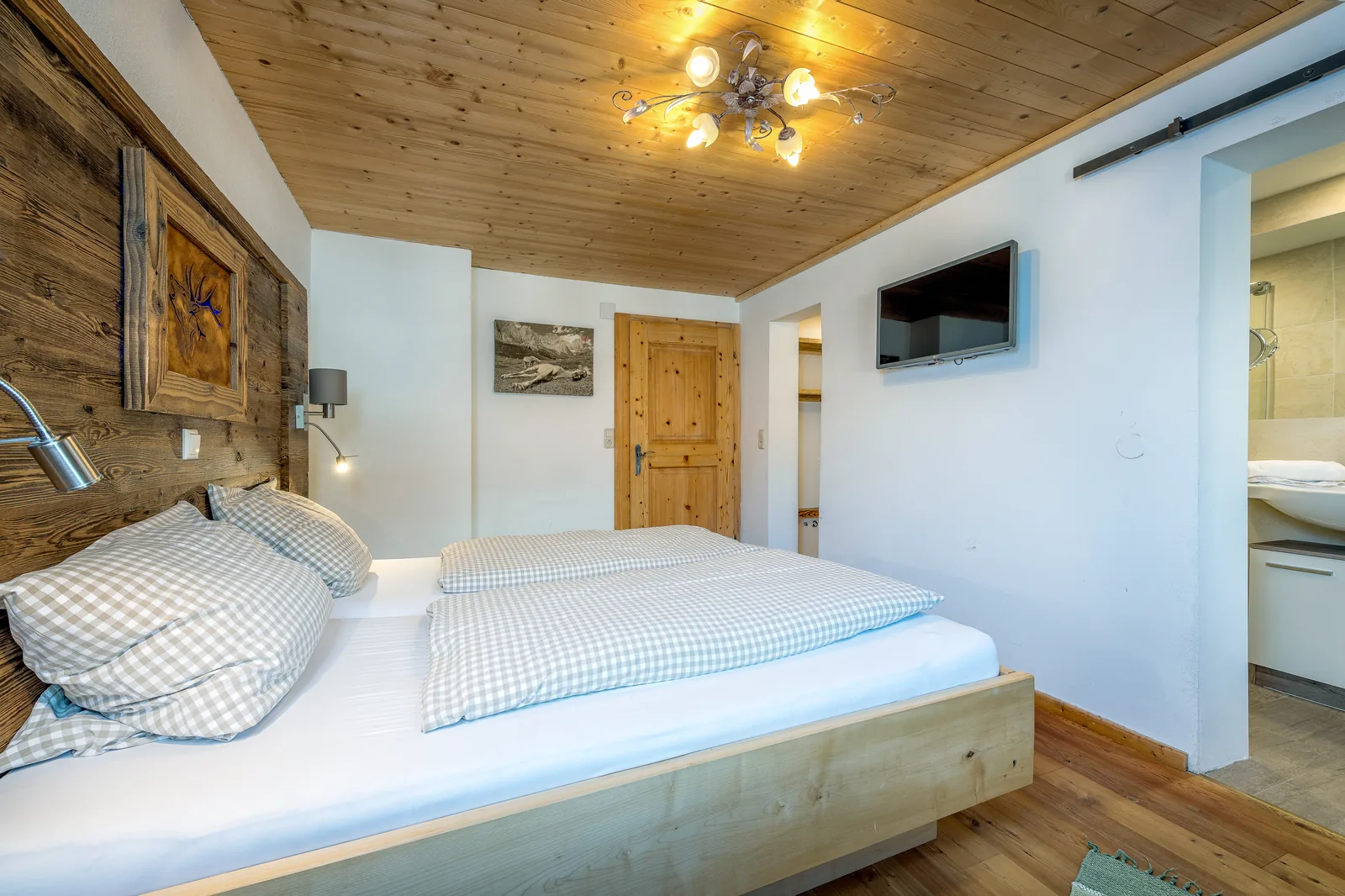 Schlafzimmer im Kaiserblick mit Altholz-Kopfteil und Blick ins angrenzende Bad