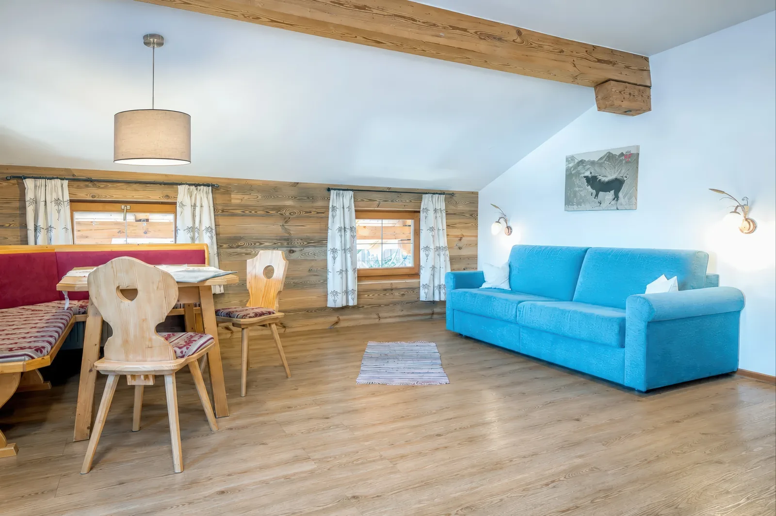 Wohnraum der Ferienwohnung Sonnblick mit blauem Schlafsofa, Eckbank und Esstisch